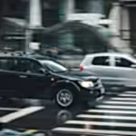 Vehicles speeding through a city street with a visible zebra crossing and blurred motion effect.
