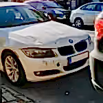 White BMW sedan with front-end damage parked on a busy city street.